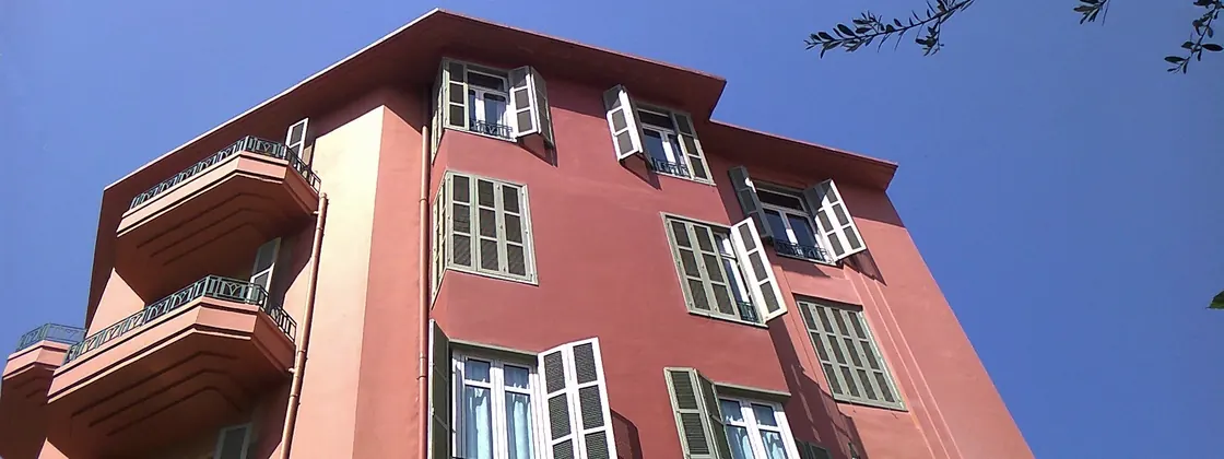 A red Achrafieh building with green shutters against a blue sky